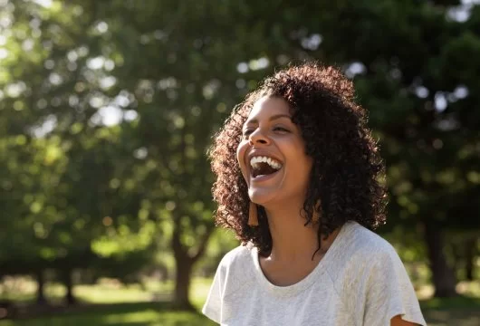 Young woman with curly hair standing outdoors and laughing