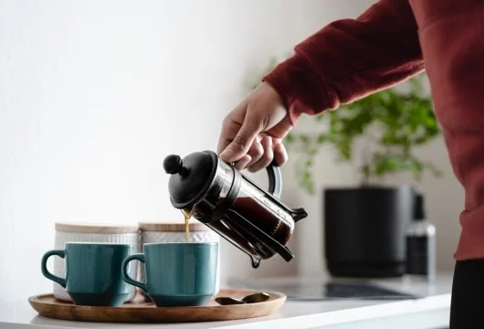 Person pouring coffee from a French press into a blue mug