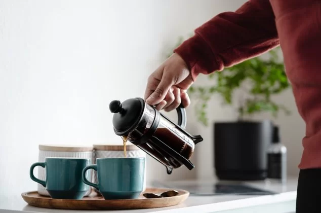 Person pouring coffee from a French press into a blue mug