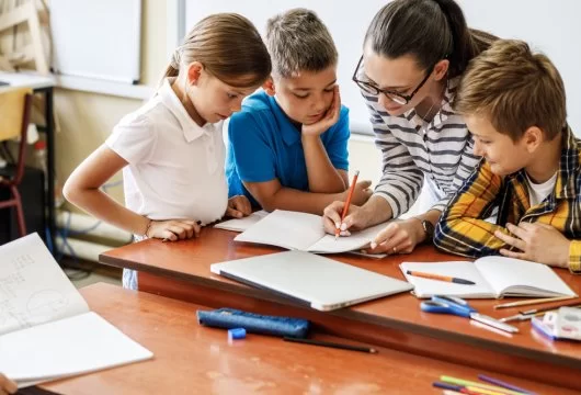 Teacher helping three elementary students with an assignment