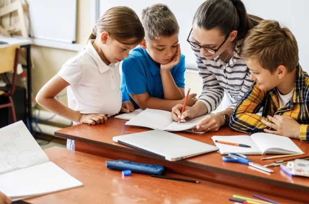 Teacher helping three elementary students with an assignment