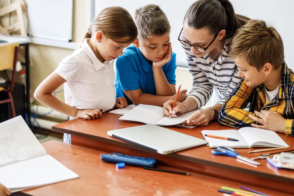 Teacher helping three elementary students with an assignment