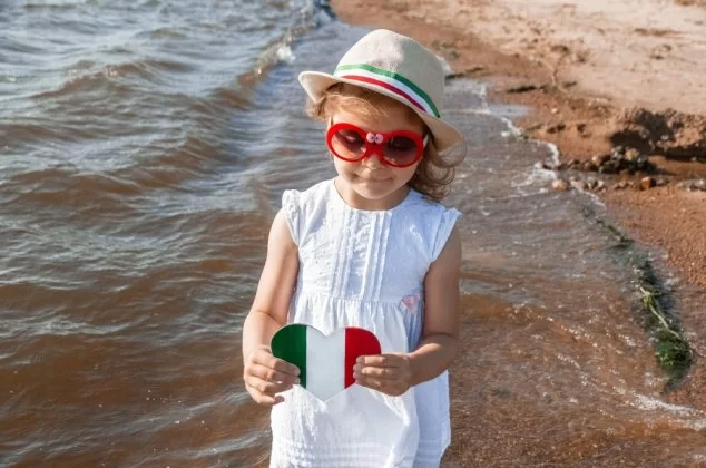 Young girl holding a heart-shaped Italian flag at the shore