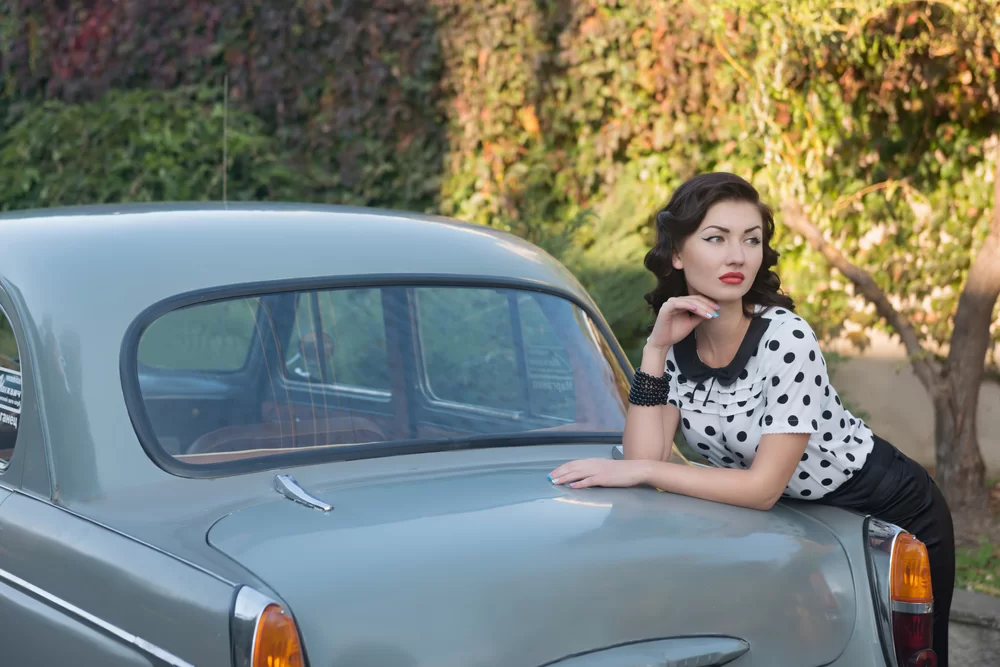 Woman wearing 1950s fashion leaning against a 1950s car