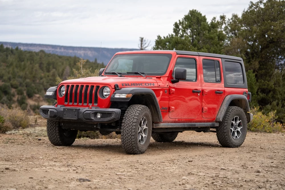Red Jeep in a dirt lot surrounded by trees