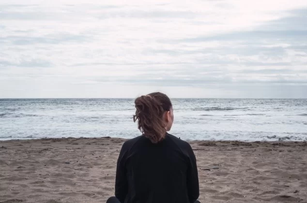 Woman sitting alone in the sand on a cloudy day at the beach
