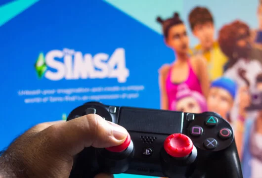 Game controller shown in front of a screen loading The Sims 4