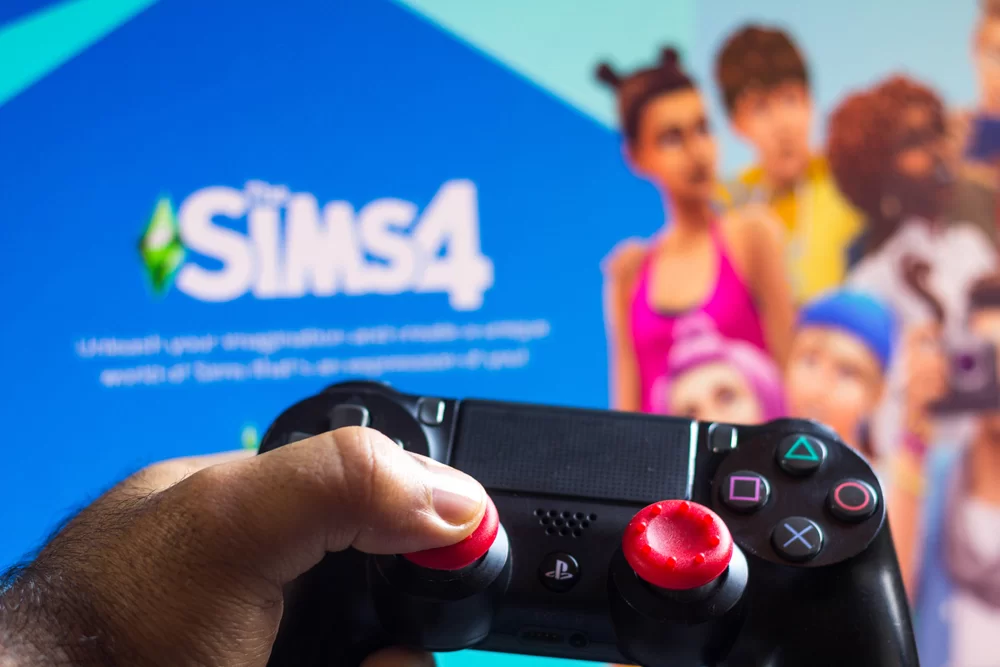 Game controller shown in front of a screen loading The Sims 4