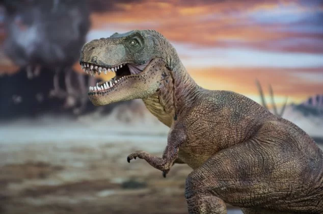 Model of a T. Rex dinosaur in front of a volcano