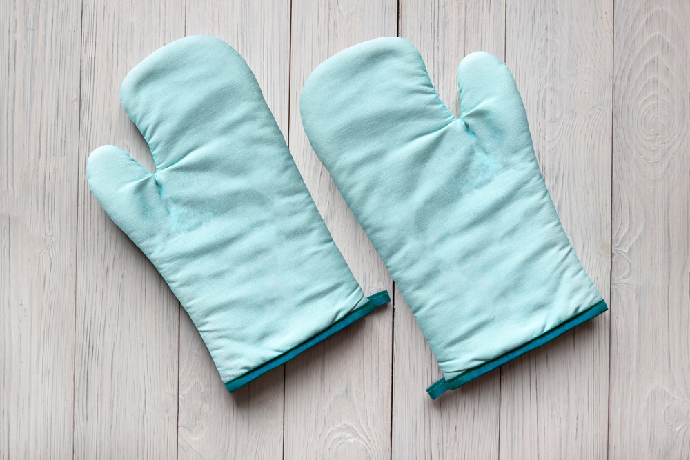 Blue oven mitts, which start with "o," resting on a wood table