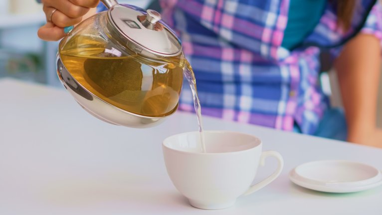 Close-up of person pouring tea from a teapot into a tea cup