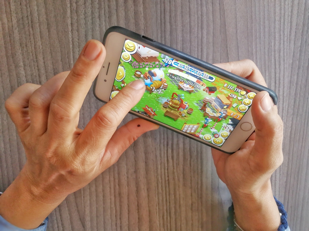 Close-up of a person's hands playing Hay Day on a smartphone