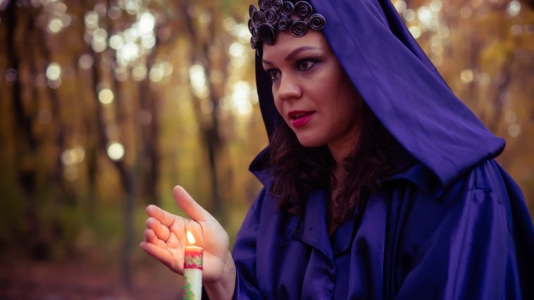 Witch wearing a purple cloak and holding a candle in the woods