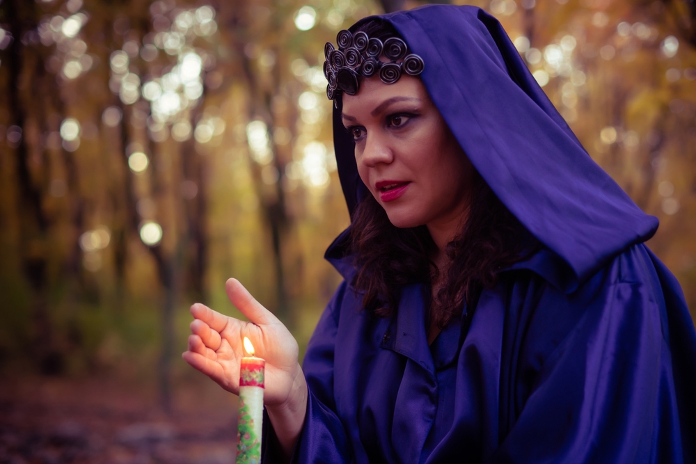 Witch wearing a purple cloak and holding a candle in the woods