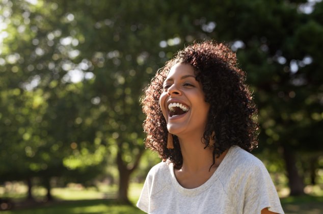 Young woman with curly hair standing outdoors and laughing