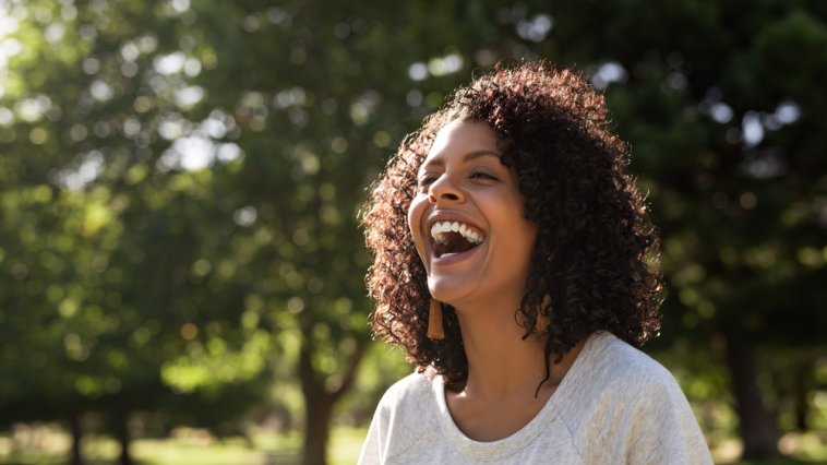 Young woman with curly hair standing outdoors and laughing