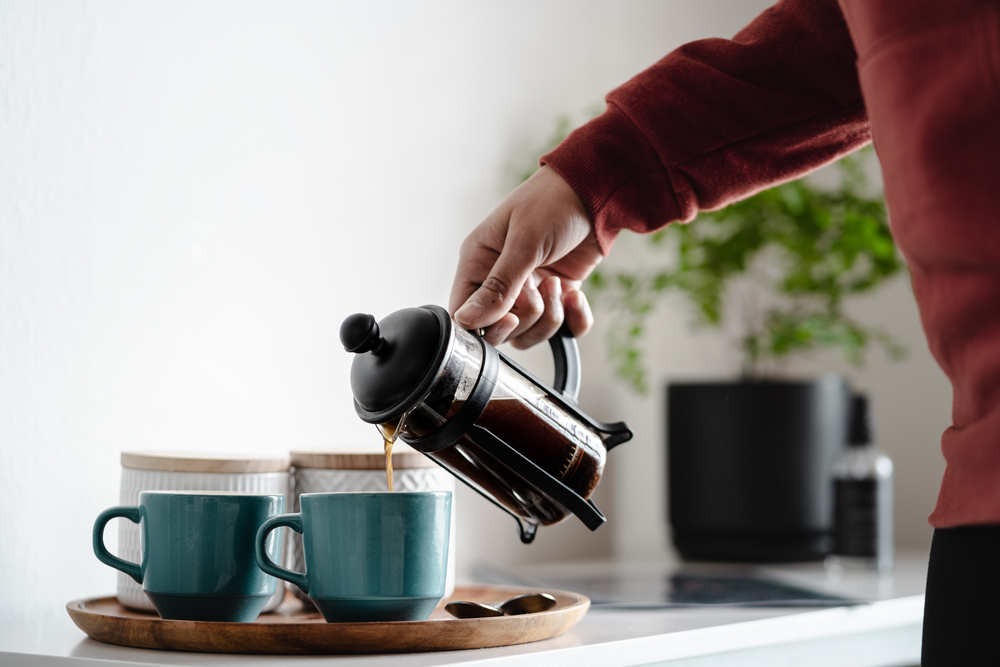 Person pouring coffee from a French press into a blue mug