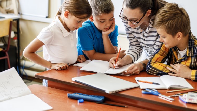 Teacher helping three elementary students with an assignment