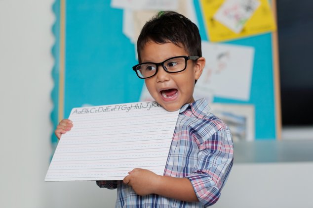 Young boy showing an alphabet practice sheet to his class for show and tell