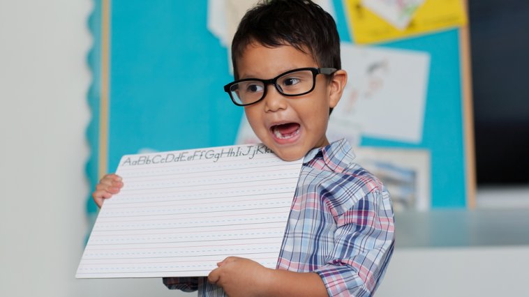 Young boy showing an alphabet practice sheet to his class for show and tell