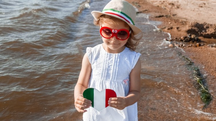 Young girl holding a heart-shaped Italian flag at the shore