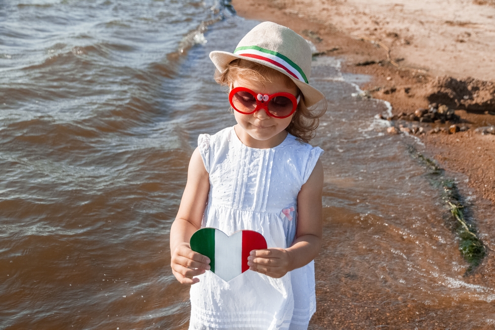 Young girl holding a heart-shaped Italian flag at the shore