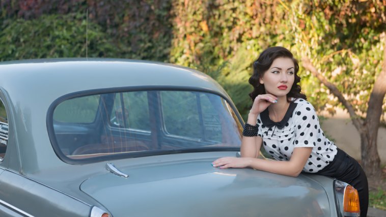 Woman wearing 1950s fashion leaning against a 1950s car