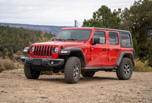 Red Jeep in a dirt lot surrounded by trees
