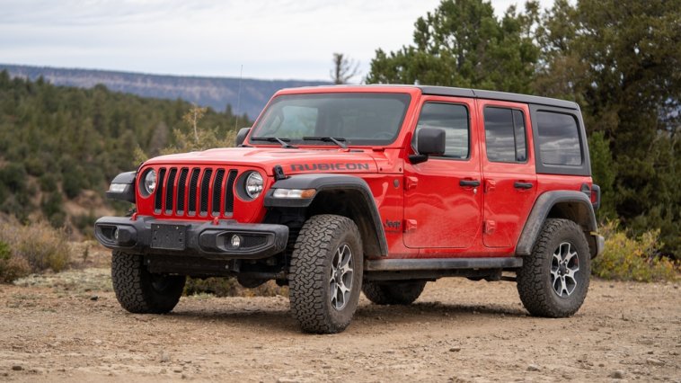 Red Jeep in a dirt lot surrounded by trees