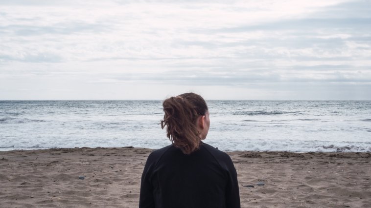 Woman sitting alone in the sand on a cloudy day at the beach