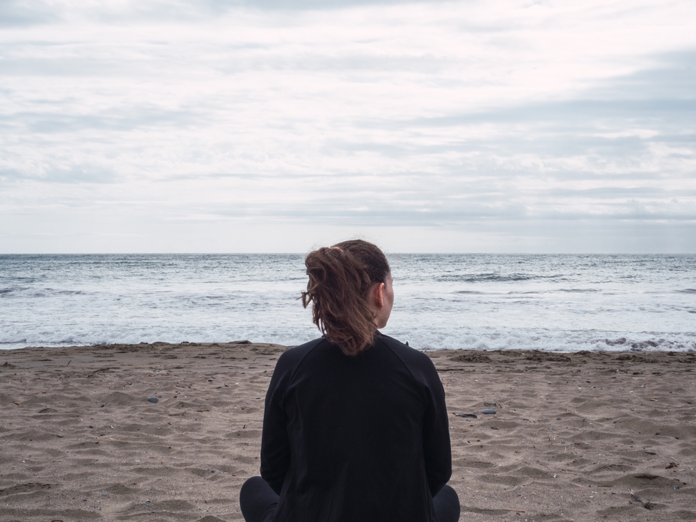 Woman sitting alone in the sand on a cloudy day at the beach
