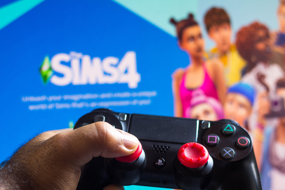 Game controller shown in front of a screen loading The Sims 4